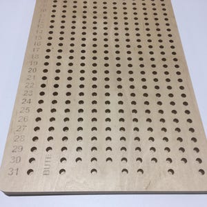 May include: A wooden pegboard with 31 rows of holes, numbered from 1 to 31. The pegboard is made of light wood and has a smooth surface. The holes are evenly spaced and are about 1.2 cm in diameter.