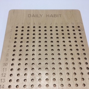 May include: A wooden daily habit tracker with a grid of holes for marking days of the month. The months are labelled across the top: January, February, March, April, May, June, July, August, September, October, November, December.