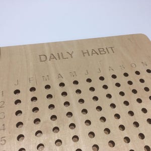 May include: A wooden daily habit tracker with holes for marking off days. The tracker has the months of the year labelled across the top and numbers 1 through 5 down the side.