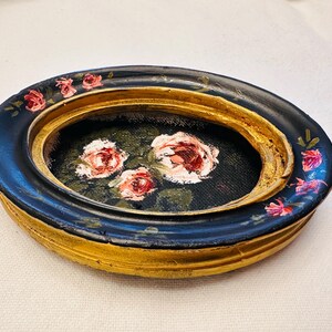 May include: A small oval trinket dish with a black and gold rim and a painted floral design of pink roses on a black background.