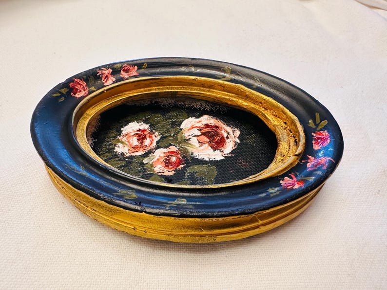 May include: A small oval trinket dish with a black and gold rim and a painted floral design of pink roses on a black background.