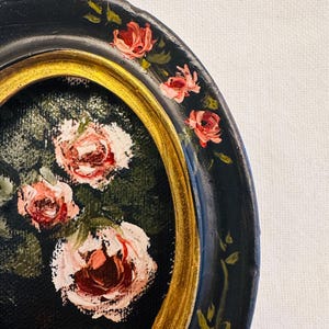 May include: A black and gold circular plate with a painted design of pink roses and green leaves. The plate has a gold rim and a black background.
