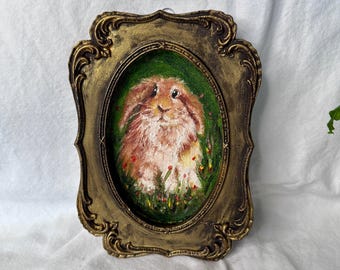 May include: An oval oil painting of a brown rabbit with long ears, set against a dark green background with small red and yellow flowers. The artwork is encased in an ornate, antique-style gold frame with intricate scrollwork and a distressed finish.