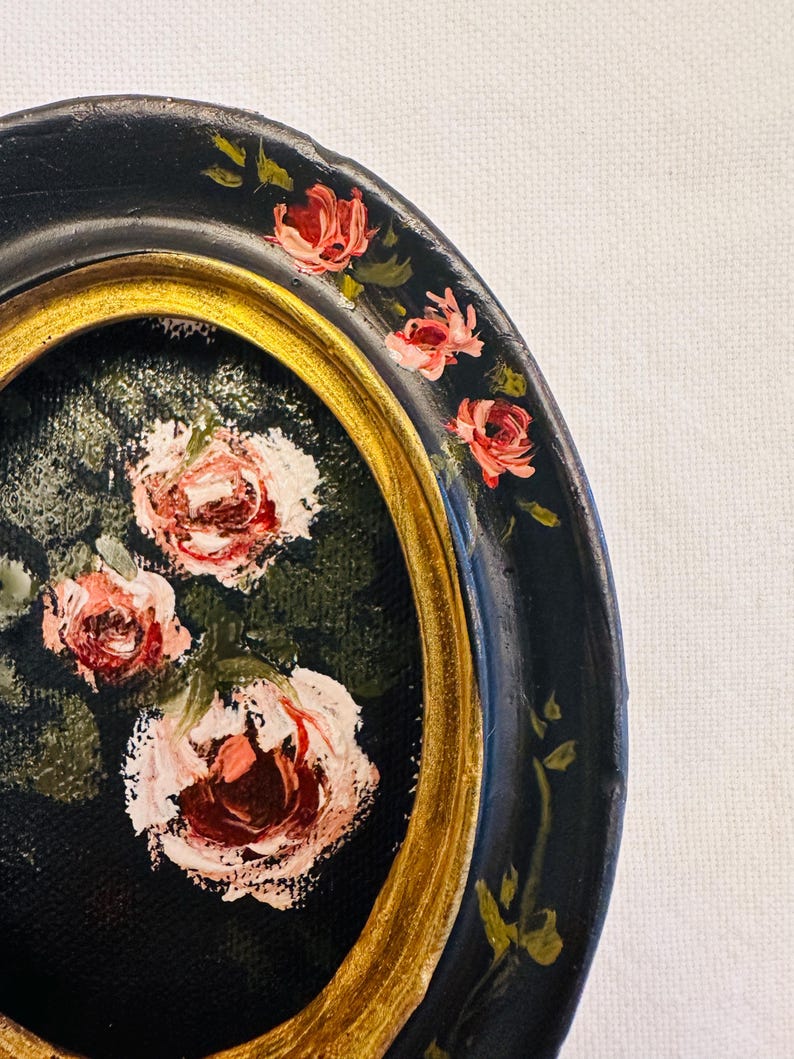 May include: A black and gold circular plate with a painted design of pink roses and green leaves. The plate has a gold rim and a black background.