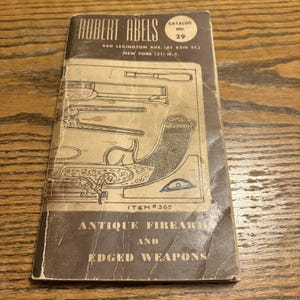 May include: A vintage catalog from Robert Abels, featuring antique firearms and edged weapons. The cover is a faded brown with the text "ROBERT ABELS" at the top, along with "CATALOG NO. 29". The catalog includes illustrations of antique weapons.