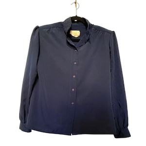 May include: A navy blue blouse with long sleeves and a mandarin collar. The blouse has a button-down front and is hanging on a black hanger. The fabric appears to be a smooth, lightweight material.