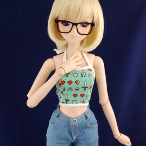 May include: A doll with blonde hair wearing black glasses, a green and white halter top with a pixelated design, and blue denim shorts.