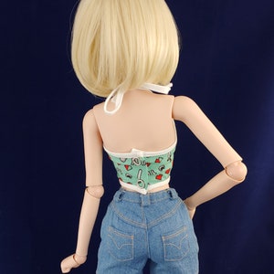 May include: A doll wearing a green and white halter top with a red and white pattern and blue denim shorts.
