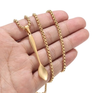 Op de afbeelding: Een goudkleurige ketting met een lepelhanger. De hanger is een gedetailleerde miniatuurlepel, hangend aan een fijne ketting. De ketting heeft een box-achtig ontwerp. De ketting wordt getoond tegen een neutrale achtergrond.