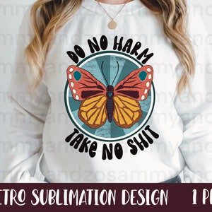 Może przedstawiać: Biała bluza z retro grafiką przedstawiającą motyla w niebiesko-żółto-czerwonych kolorach. Tekst "Do No Harm Take No Shit" jest napisany w okrągłym wzorze wokół motyla.