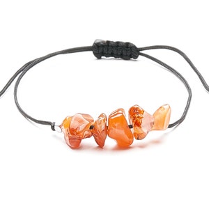 Puede incluir: Un brazalete ajustable simple con un cordón negro y un grupo de piedras de cornalina naranja.