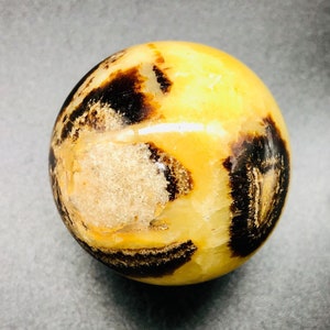 May include: A polished sphere of yellow and brown banded agate. The agate has a natural, organic pattern.