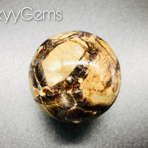 May include: A polished sphere of brown and beige tiger iron with a swirling pattern. The sphere is approximately 5 cm in diameter.