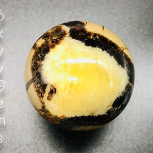 May include: A polished sphere of yellow and brown banded agate. The agate has a smooth, polished surface and a natural, organic pattern.