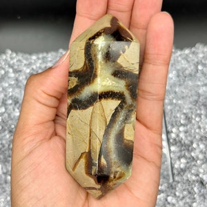 May include: A brown and black banded agate crystal point, also known as a septarian nodule, in the shape of a double-terminated point.