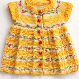 May include: A yellow knitted dress with short sleeves and a round neckline. The dress features a pleated skirt and is adorned with red buttons down the front. The bodice has a floral pattern in white, green, and pink.