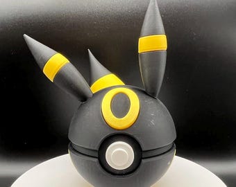 May include: Black and yellow 3D printed Pokemon figurine of a Pokeball with a black and yellow Eevee on top.