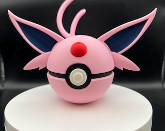 May include: A pink and black decorative ball with a red dot and white circle. The ball has pink wings and two curved pink antennae. The design is reminiscent of a popular animated character.