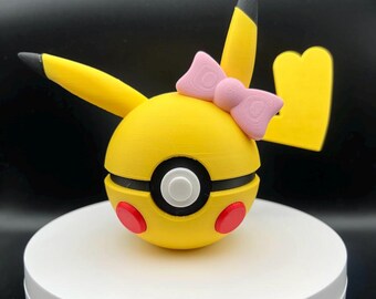 May include: A yellow and black Pokeball with a pink bow on top. The Pokeball is a popular collectible toy.