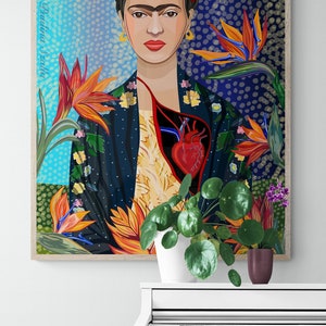 May include: A framed illustration of Frida Kahlo with a red heart and flowers. The illustration is in a blue, green, and orange color scheme. The frame is wood and has a light brown color.