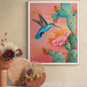 May include: A framed painting depicting a blue hummingbird in flight, approaching a pink and orange flower, set against a pink and peach gradient. A turquoise cactus is also featured. The artwork is signed "Spalle".