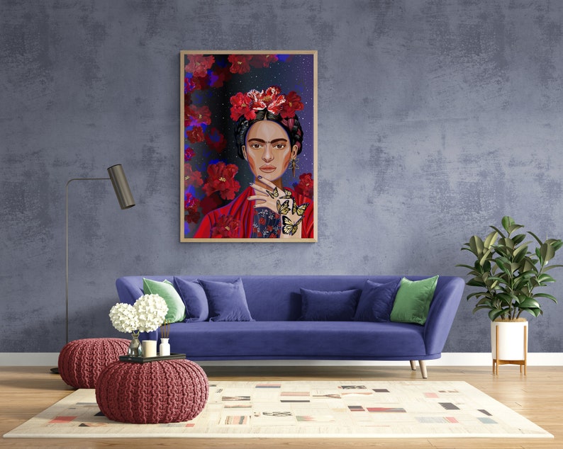 May include: A framed illustration of Frida Kahlo with a floral crown and butterflies on a blue background. The illustration is hanging on a blue wall above a blue sofa with green throw pillows.