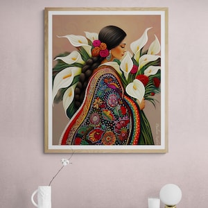 May include: A woman in a colourful embroidered dress holds a bouquet of white calla lilies. The flowers are arranged in a fan shape, with the woman's hand visible at the bottom of the bouquet. The woman's hair is long and dark, and she is wearing a flower in her hair. The background is a light brown colour.