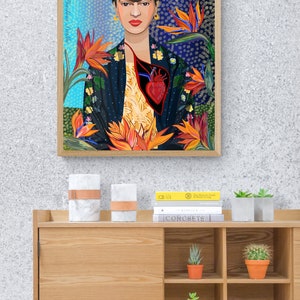 May include: A framed print of a colorful illustration of Frida Kahlo with a heart in her chest and flowers surrounding her. The text "Frida Kahlo" is written vertically on the left side of the frame.