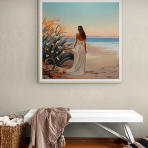 May include: A framed painting of a woman in a white dress walking on a beach with a sunset in the background. The beach is sandy and the water is blue. There are orange flowers in the foreground.