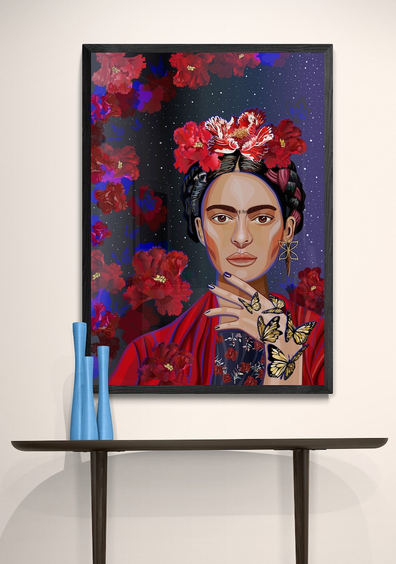 May include: A framed illustration of Frida Kahlo with a red floral crown and butterflies on her hand. The background is a dark blue with red flowers.