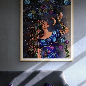 May include: A digital illustration of a woman with long brown hair wearing a blue dress with floral embroidery. She is reaching up towards a crescent moon with stars in the background. The artwork is framed in a wooden frame.