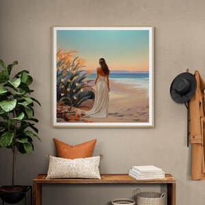 May include: A framed painting of a woman in a white dress walking on a beach with a sunset in the background. The beach is sandy and there are waves in the ocean. There are orange flowers in the foreground.
