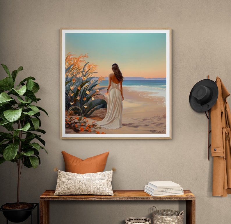 May include: A framed painting of a woman in a white dress walking on a beach with a sunset in the background. The beach is sandy and there are waves in the ocean. There are orange flowers in the foreground.