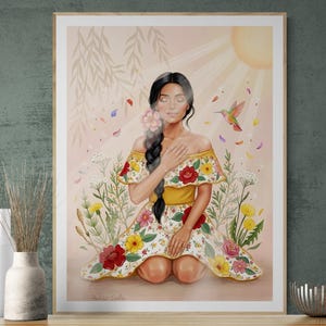 May include: A framed art print featuring a woman in a floral dress, kneeling in a field of wildflowers. A hummingbird flies near her, with sun rays and falling petals. The artwork has a soft, warm color palette.