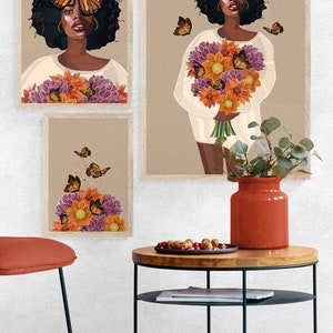 Puede incluir: Tres impresiones enmarcadas con una mujer de cabello oscuro y una mariposa sobre sus ojos sosteniendo un ramo de flores. La mujer lleva una camisa blanca. Las impresiones est&aacute;n en una pared blanca con una mesa de madera y un jarr&oacute;n rojo con una planta verde.