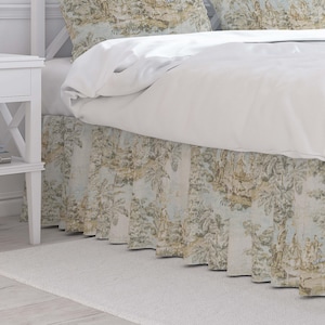 May include: A bed with a white comforter and a patterned bed skirt. The bed skirt features a light blue and beige toile design with trees and figures. A white nightstand is visible on the left.