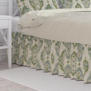 May include: A bed with a cream-colored comforter and patterned bed skirt. The bed skirt features a repeating design in shades of green and blue on a cream background. A white nightstand is visible on the left side of the bed.