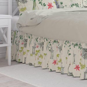 May include: A bed skirt with a cream-colored background featuring a repeating pattern of cranes, pagodas, and floral elements in green, red, and gray. The bed skirt has a pleated design and is part of a bedding set.