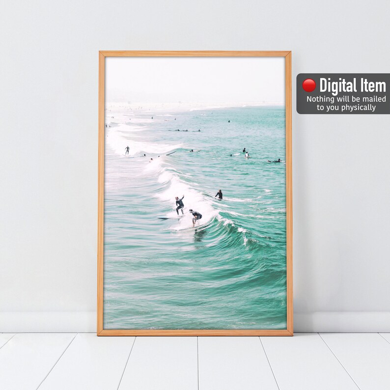 May include: Framed print featuring a serene ocean scene with surfers riding waves. The turquoise water contrasts with the light brown frame. The image includes the text "Digital Item - Nothing will be mailed to you physically."