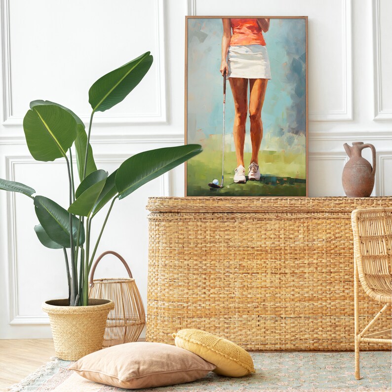 May include: A woven wicker storage trunk with a light brown finish. The trunk is decorated with a painting of a woman playing golf. The painting is framed in a light wood frame. The trunk is sitting on a rug with a green and brown pattern.