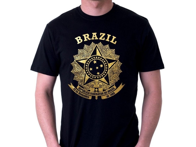 May include: Black t-shirt with a gold graphic of the Brazilian coat of arms. The graphic includes a star with a blue circle and stars, a banner with the text "REPUBLICA FEDERATIVA DO BRASIL", and the dates "15 de Novembro de 1889".