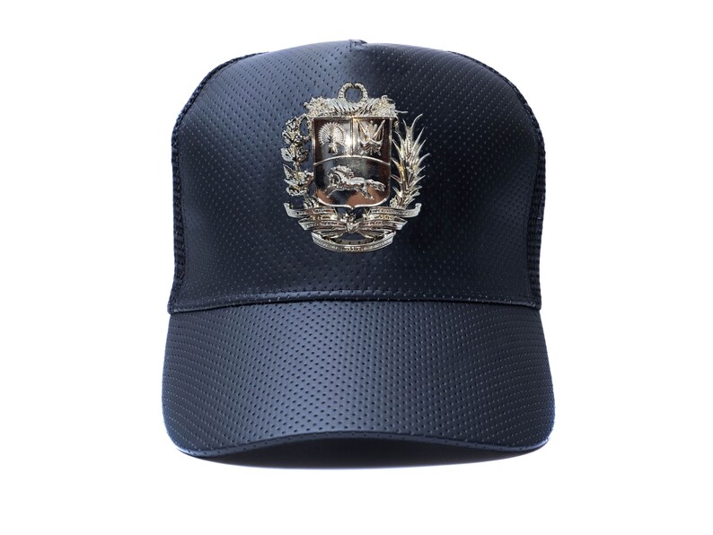 May include: A black leather trucker hat with a gold-colored emblem featuring a coat of arms. The hat has a mesh back and a curved brim.