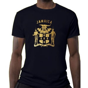 May include: A navy blue t-shirt featuring a gold foil print of the Jamaican coat of arms. The coat of arms depicts a lion, a crocodile, and the text "Jamaica".