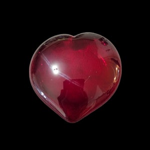 May include: A deep red glass heart shaped paperweight. The glass is smooth and shiny.