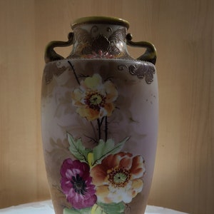 May include: A vintage ceramic vase with two handles, featuring a floral design with pink, yellow, and brown flowers on a light brown background.