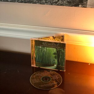 May include: A CD case with a green and white image of a bamboo forest path. The title of the CD is "Relax and be Still" with the subtitle "Guided Meditations with Joseph Men".