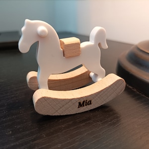 May include: White wooden rocking horse with a saddle and the name "Mia" engraved on the base.