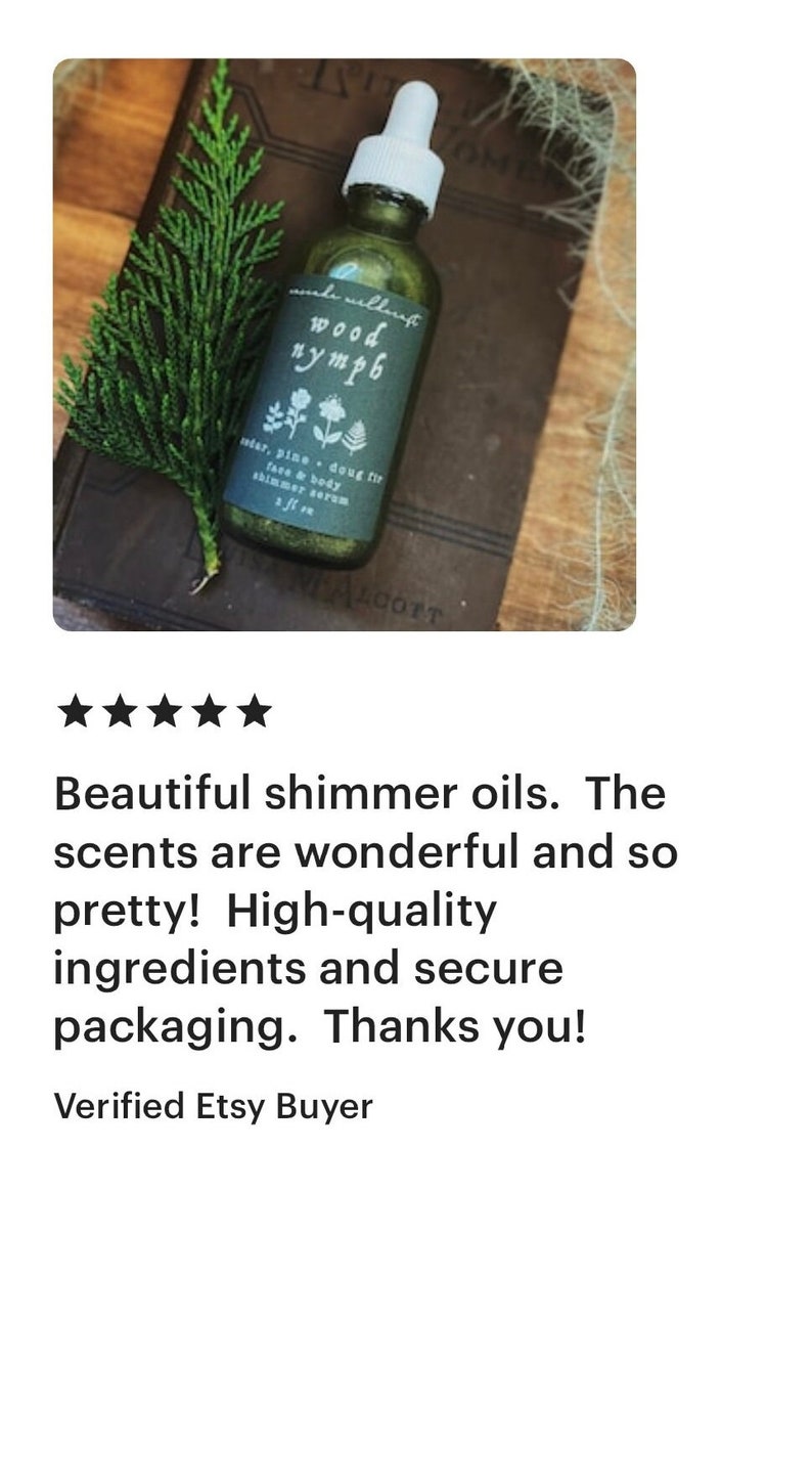 以下が含まれることがあります： 黒いラベルに「wood nymph」と「cedar, pine - doug fir face & body shimmer serum 1 fl oz」と書かれた、小さな透明なガラス瓶。瓶は茶色の表面に緑の葉っぱと一緒に置かれている。