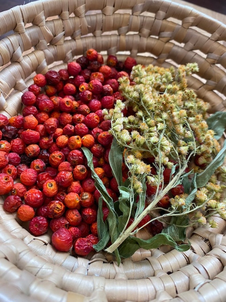 May include: A wicker basket filled with dried red berries and a sprig of dried green foliage.