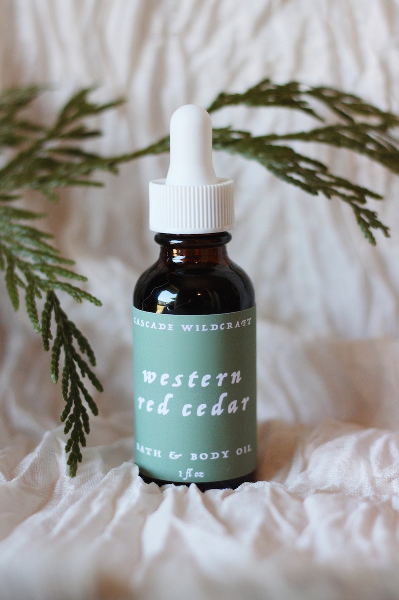 May include: A brown glass bottle with a white dropper top and a green label that reads "CASCADE WILDCRAFT western red cedar BATH & BODY OIL 1 fl oz".